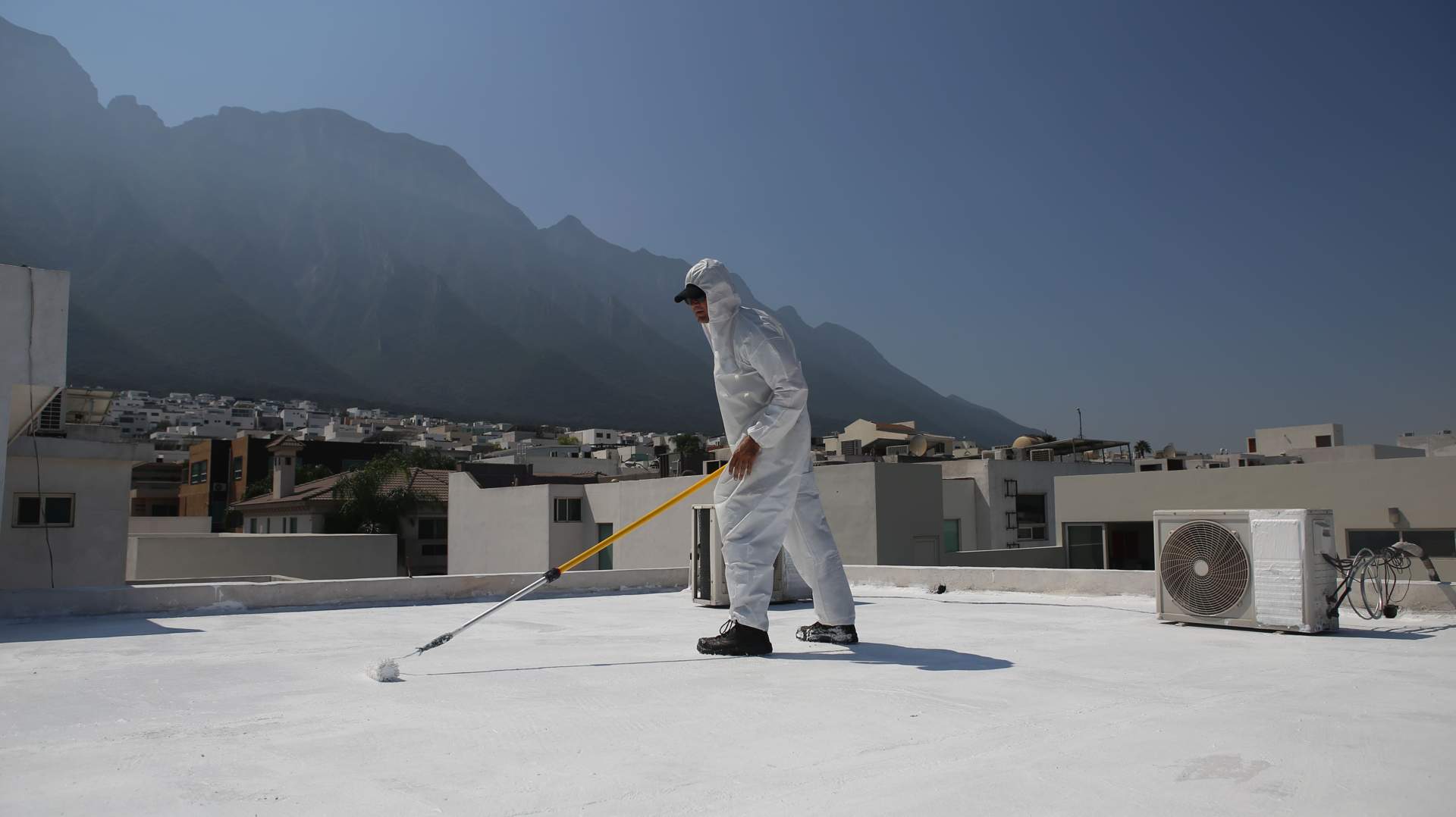 Un trabajador impermeabilizando un techo con pintura elastomerica mientras usa equipo de proteccion