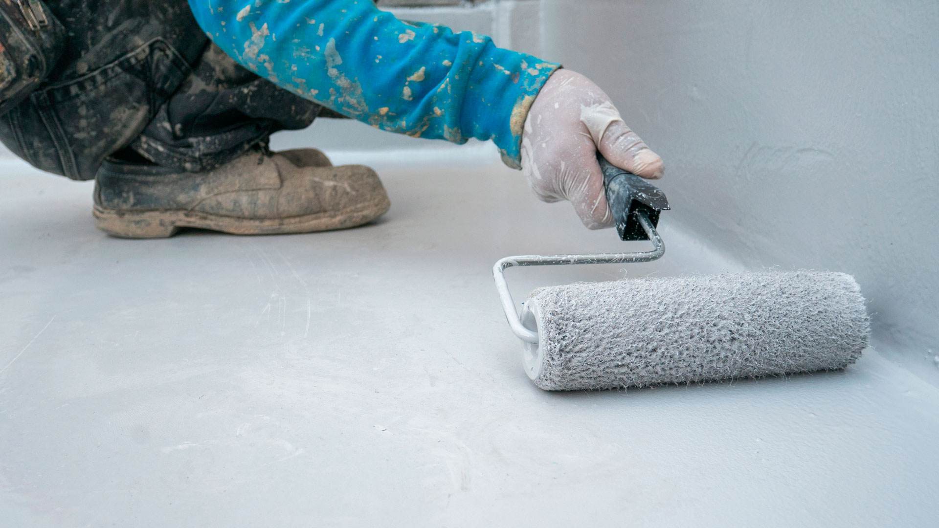  Como pintar un suelo ceramico interior_Hombre aplicando impermeabilizante a un suelo con un rodillo