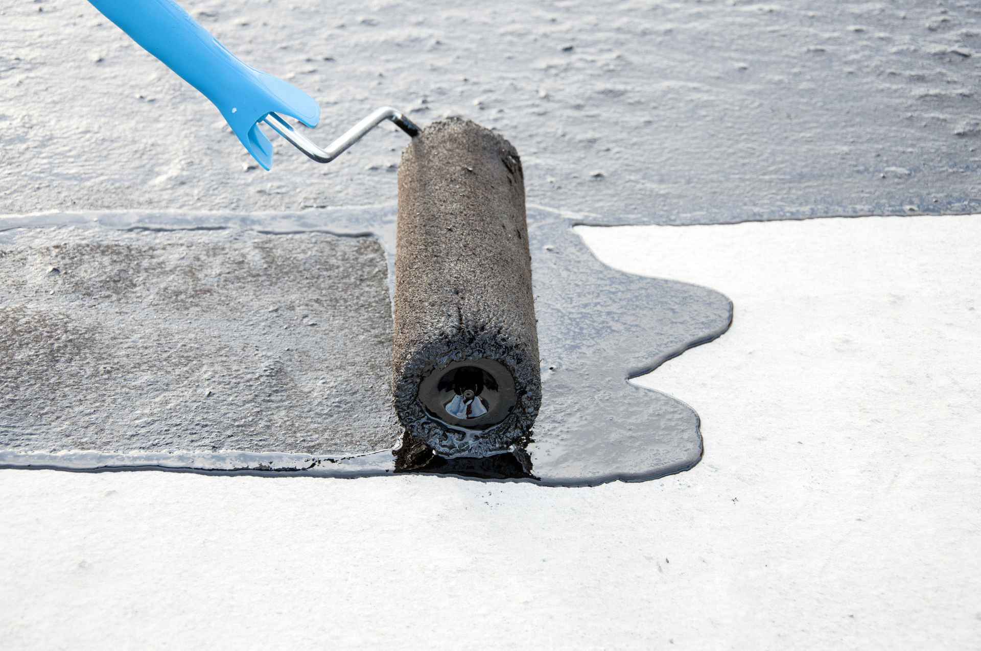 Acercamiento a un rodillo de mano largo durante la aplicacion de impermeabilizante negro sobre un techo